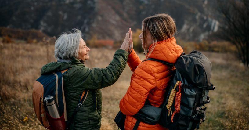 Dva turisté v outdoorových bundách si dávají high five na pozadí hor