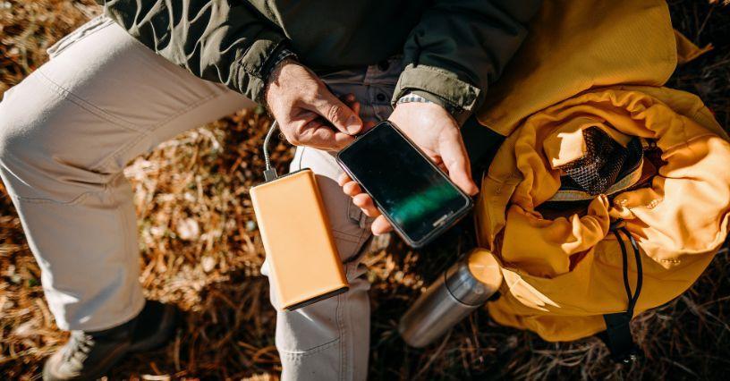 Osoba nabíjí telefon pomocí přenosné powerbanky vedle žlutého batohu